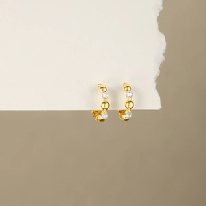 Detailed close-up of gold beaded hoop earrings with white pearls on art paper background