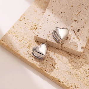 Macro shot of polished silver heart-shaped earrings on natural stone with elegant reflection