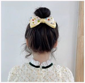 Rear view of a model wearing the yellow polka dot fabric bow hair clip on long hair