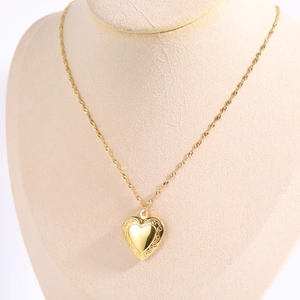 Detail showing an openable gold heart locket necklace with embossed floral patterns on chain
