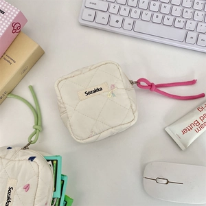 Close-up of a white quilted sanitary storage pouch with a colorful zipper pull on a desk