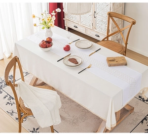 Detailed view of beige tablecloth with white hollow-out lace table runner in a home dining setup
