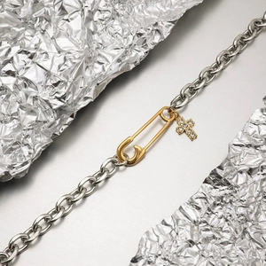 Gros plan détaillé sur un pendentif épingle de sûreté bicolore et croix sur chaîne acier