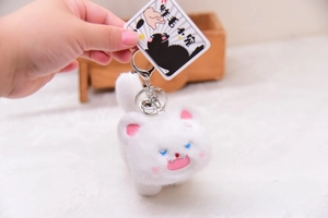 Close-up of white fluffy cat plush keychain with vivid blue eyes and metal bell detail