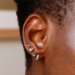 Detailed view of S925 silver helix piercings with green gemstone and diamond accents