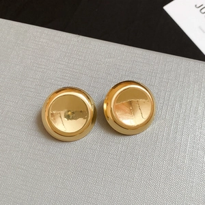 Close-up of minimalist round golden earrings with a polished metallic finish on a textured surface