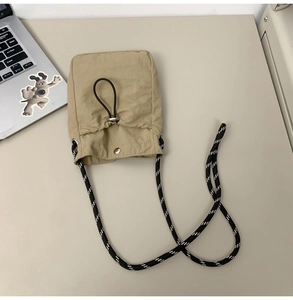 Detail of beige drawstring crossbody bag with black and white woven rope strap on desk
