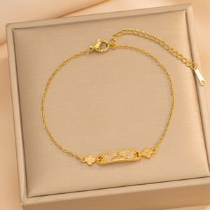 Elegant gold zircon bracelet featuring a rectangular plaque and clover charms on a jewelry box