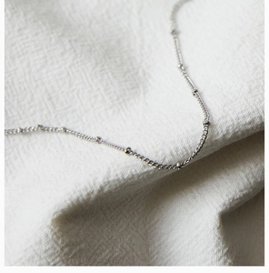 Macro detail of silver steel chain necklace with small beads on white textured fabric