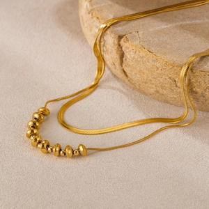 Detail of a layered golden titanium steel necklace with snake chain and metallic beads