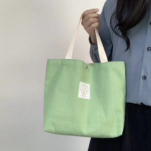 Detail of light green canvas tote bag featuring a cute dog patch and white fabric handles