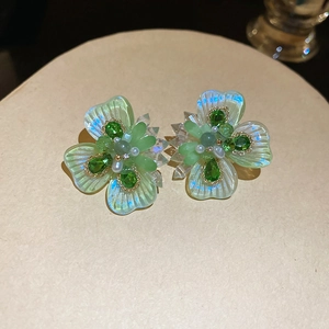 Detailed view of green crystal flower earrings with pearl center on a beige pedestal