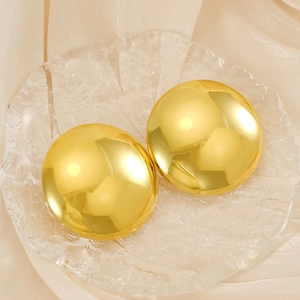 Detail of golden geometric round hoop earrings on a textured glass plate with soft shadows