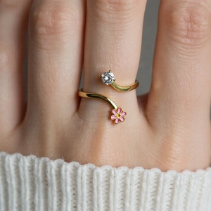Close-up of gold open ring with pink enamel flowers and a clear round zircon stone