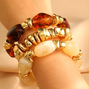 Retro multi-layer resin and golden bead bracelet set worn against champagne silk fabric