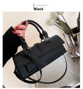 Detail view of the black leather handbag featuring dual handles and a slim shoulder strap