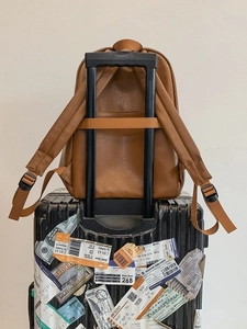 Brown soft leather backpack with luggage strap fixed on a black suitcase trolley