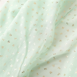 Macro shot of light mint green fabric with golden leaf pattern and soft pleats