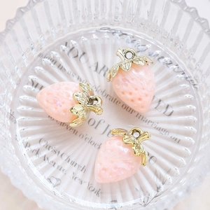 Detailed view of three pink acrylic strawberry charms with gold leaves in a glass tray