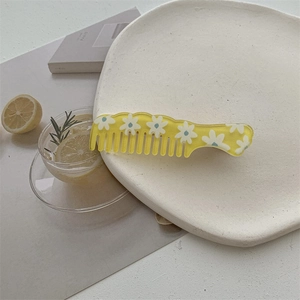 Close-up of a yellow floral resin hair comb with daisy patterns on a ceramic plate