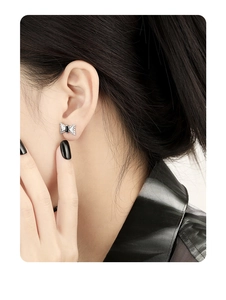 Close-up of S925 silver bow stud earrings with black gem on ear for a chic look