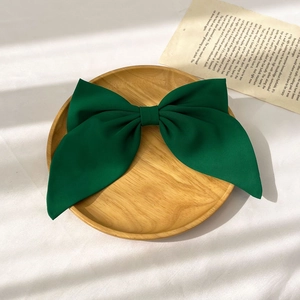 Detailed texture of a large dark green fabric bow hair clip on a minimalist wooden tray