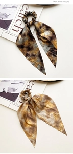 Close-up of golden brown marble pattern satin hair scrunchie with long ribbons on white desk