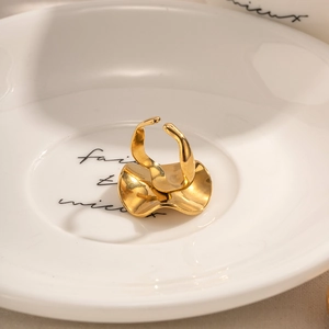 Detailed close-up of a gold wave-shaped adjustable stainless steel ring on a ceramic tray