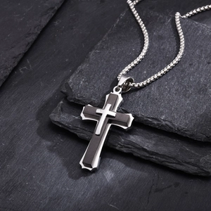 Macro shot of tiered silver and black cross pendant on a textured dark stone background