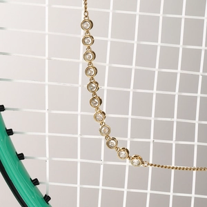 Détail d'un bracelet de tennis doré serti de zircons posé sur une raquette de tennis
