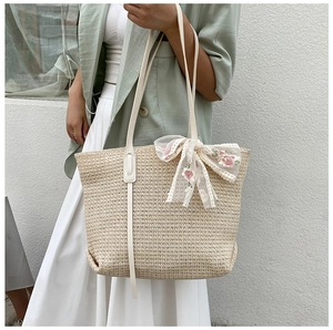 Detail of beige straw tote bag featuring white leather straps and a pink lace floral bow