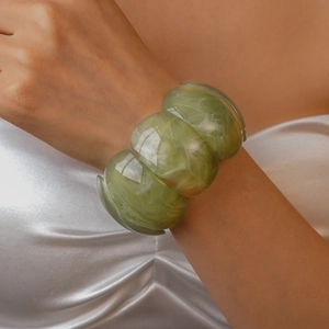 Detail of light green marble acrylic wide bracelet worn on model over white silk fabric