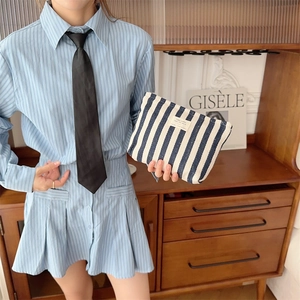 Detail of blue and white striped canvas toiletry bag held by a model in a casual outfit