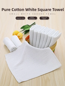 Detail of soft white cotton square towels folded in a woven basket on a wooden table