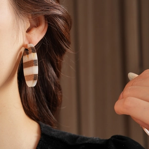 Detail of a C-shaped earring with wood and resin stripes on a model's ear