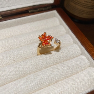 Macro detail of 18k gold maple leaf ring with orange cubic zirconia on white jewelry box