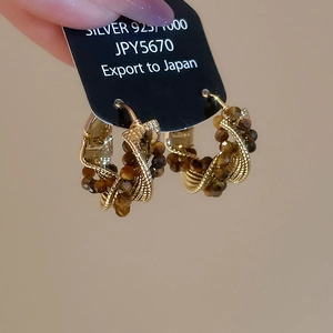 Detail of twisted gold earrings with tiger eye beads held against a minimalist wall