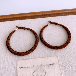 Detailed close-up of leopard print velvet hoop earrings on a vintage fabric background