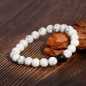 Handmade white turquoise beaded bracelet with matte black agate bead on a wooden surface