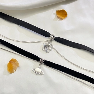Detail von schwarzem Samt-Choker mit silbernen Blumen- und Saturn-Anhängern auf weißer Seide