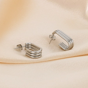 Detail of silver triple-layered ribbed metal earrings on champagne silk fabric background