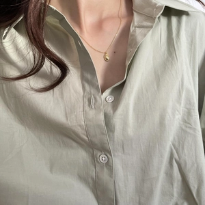 Close-up of minimalist gold oval pendant necklace on a model wearing green linen