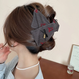 Detail view of denim bow hair claw clip with red embroidery worn on an updo hairstyle