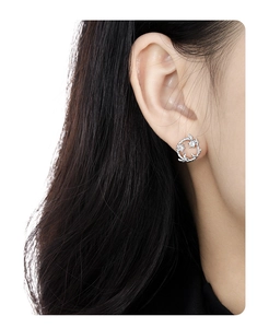 Detailed view of silver wreath stud earrings with zircons on a model's ear