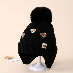 Detailed knit texture and brown bear embroidery on a black winter trapper hat with pom