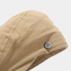 Close-up of cotton twill beret with silver metallic logo badge and stitching detail