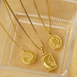 Trois colliers dorés avec pendentifs soleil et lune dans un plateau en verre
