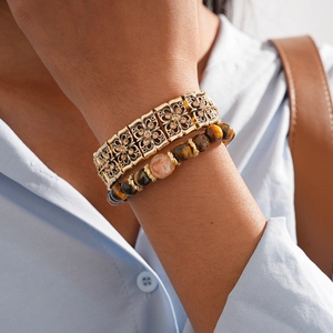 Detail of layered gold flower bangle and tiger eye bead bracelet set on wrist