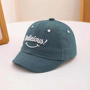 Close-up of Delicious embroidery and smiley face on dark teal toddler cotton cap
