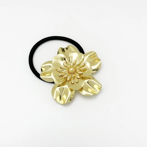 Detailed macro view of the golden metal flower ornament on a black elastic hair tie